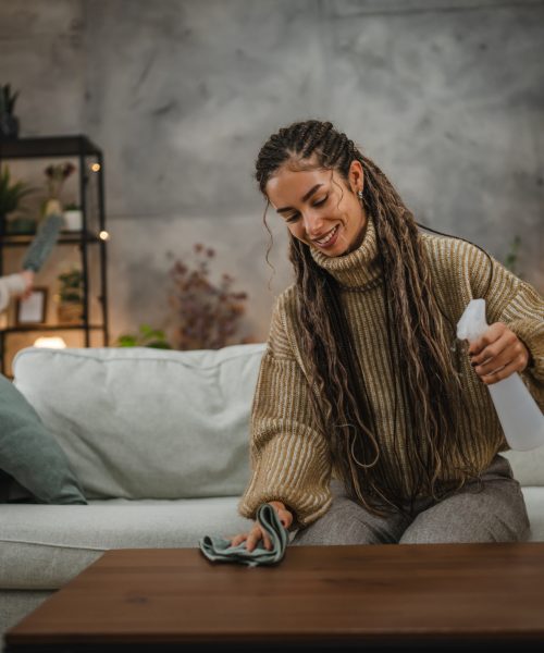 Young woman wipe dust use spray and green fabric cleaning on table in the living room